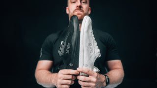 Mann hält den neuen Barfuß Trainingsschuh, den Lifters Bare One in den Farben weiß und schwarz in die Kamera