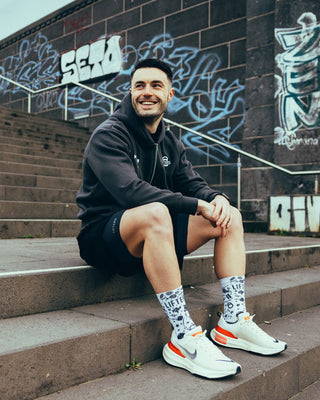 Athlet trägt den grauen Hybrid Essential Zip Hoodie und lächelt.